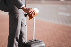 Close-up shot of a black businessman's hand holding a passport and luggage handle