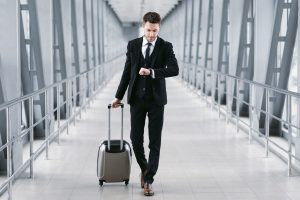 Boarding Time. Confident man checking time on watch, walking with suitcase in airport, going to departure gate