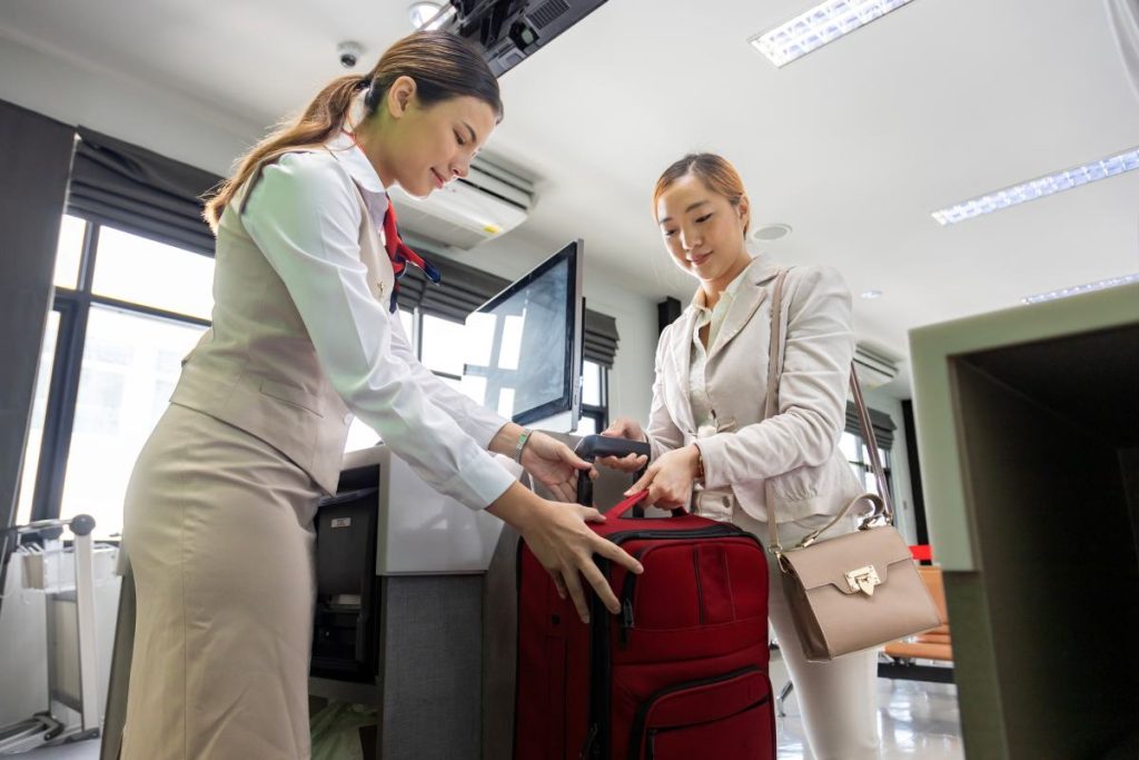 Asian passenger is checking in her big luggage bag to airline ground crew at departure gate into the airplane