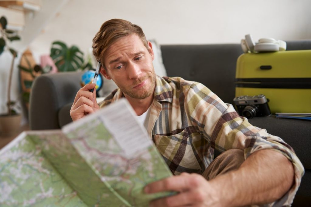 Portrait of man, tourist looking confused at travel map, shrugging, cant decide on route, choosing the road for travelling