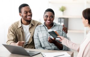Travel Agent Giving Tickets To Happy Black Travelers Couple Sitting In Tour Agency Office
