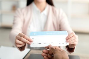 Female Travel Agent Giving Ticket To Unrecognizable Client Sitting In Tour Agency Office