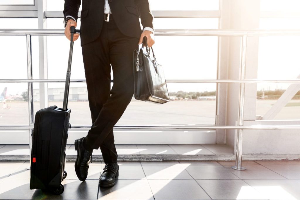 Cropped of businessman standing by window in airport, holding luggage, copy space