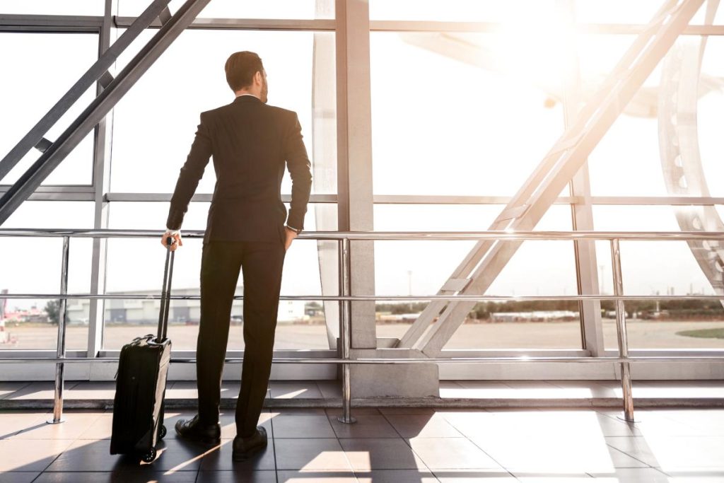 Rear view of businessman with suitcase standing next to window at airport