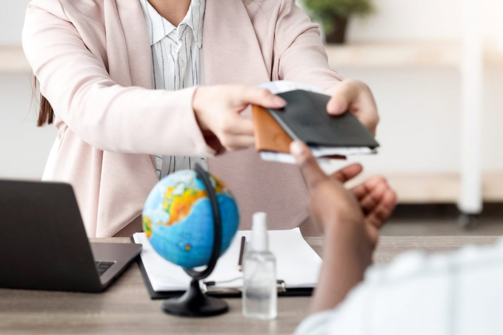 Travel Agency. Female Manager Giving Booked Tickets To African American Tourists Couple Sitting In Modern Office