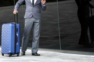 Businessman with suitcase using smartphone while outdoors