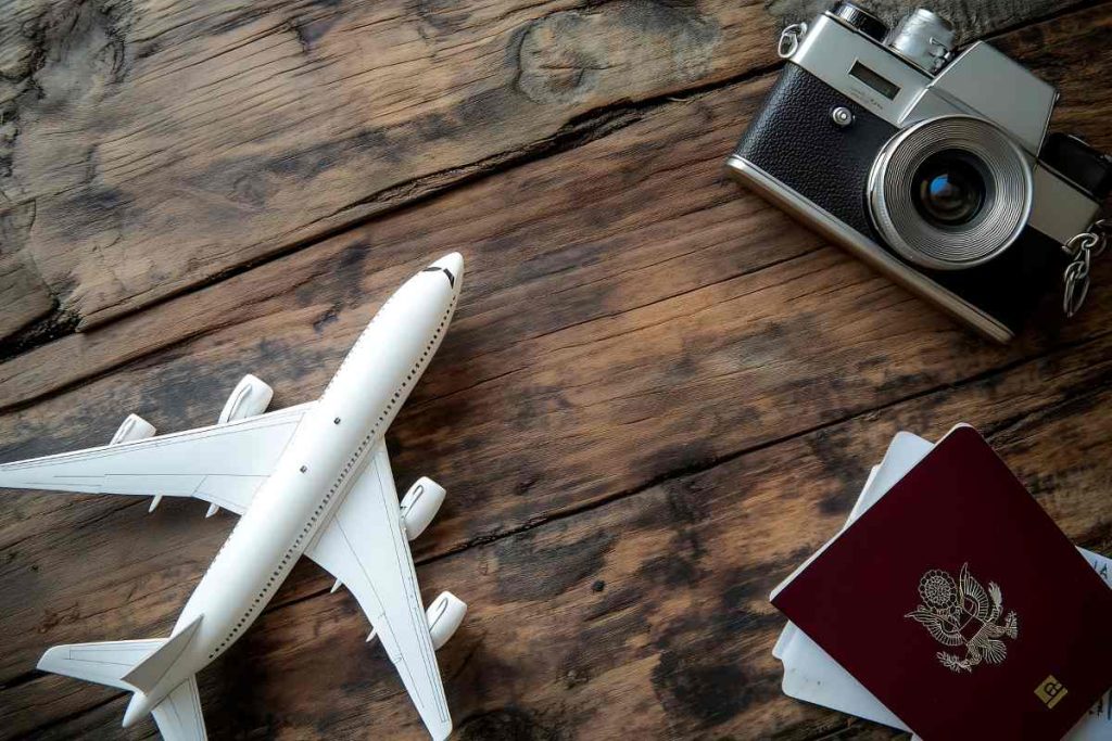 A passport a camera and a model airplane are positioned on a wooden surface suggesting a preparation for travel